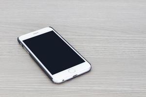 Teléfono inteligente con pantalla en blanco acostado sobre una mesa de madera gris foto
