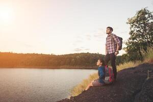 Couple having rest on the top of mountain below lake during sunset. photo