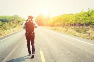 Young woman hitchhiking carrying backpack walking on the road. photo