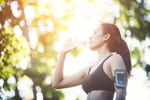 Young woman taking a break during running. Drinking water from bottle. photo