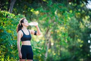 Young woman taking a break during running. Drinking water from bottle. photo