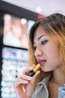 Hermosa joven seleccione lápiz labial de color para comprar en el centro comercial foto