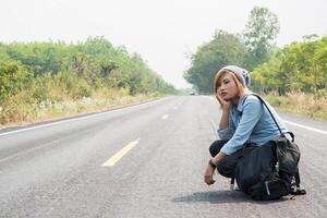 Young woman hitchhiking carrying backpack sitting on the road photo