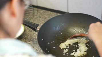 Mujer revuelva la cebolla picada en una sartén en la cocina