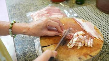 la donna anziana taglia la pancetta per preparare l'ingrediente della pasta in cucina video