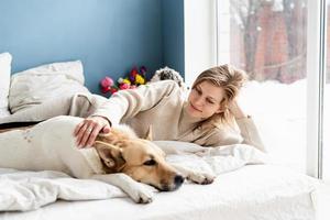 Happy young woman lying in the bed with her dogs photo