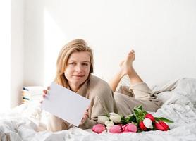 mujer acostada en la cama en pijama con ramo de flores de tulipán foto