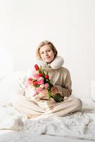 Sleepy woman sitting in bed wearing pajamas and pillow over the neck photo