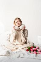 Sleepy woman sitting in bed wearing pajamas and pillow over the neck