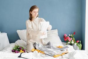 Young woman organizing clothes sitting on the bed at home