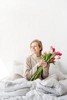 woman sitting on the bed wearing pajamas holding tulip flowers bouquet photo