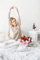 Happy woman sitting on the bed wearing pajamas stretching photo