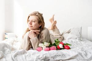Happy woman lying on the bed holding tulip flowers bouquet photo