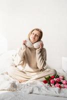 Sleepy woman sitting in bed wearing pajamas and pillow over the neck photo