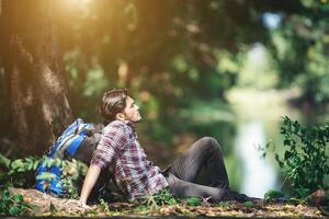 Young tired with backpack sitting on the grass  resting during hikes. photo