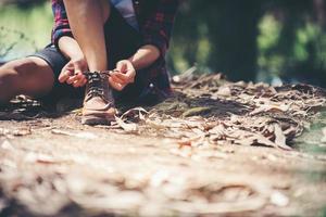 woman hiker stops to tie her shoe on a summer hiking trail in forest.
