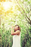 Young woman wearing white dress drinking water in the green forest. photo