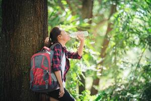 Woman a break drinking a bottle of water during hiking in the forest. photo