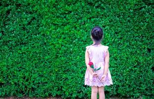 little girl in dress stand back and holding a red rose in the park photo