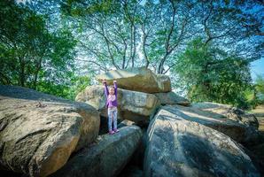 little girl standing with raised hands on rock and tree background photo