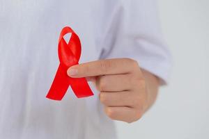 young woman's hand holding red breast cancer and AIDS awareness ribbon photo