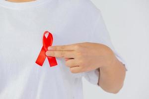 Mano de mujer joven sosteniendo cinta roja de concienciación sobre el sida y el cáncer de mama foto