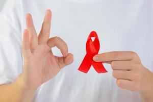 young woman's hand holding red breast cancer and AIDS awareness ribbon photo