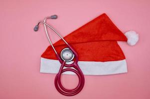 A santa claus hat with a pink stethoscope on the pink background photo