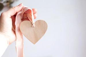 Wooden heart on pink ribbon. Hand holding wooden heart. Copy space. photo