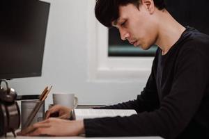 Young handsome asian man reading book at work desk late at night photo