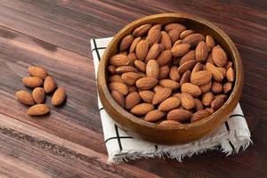 almendras en cuenco de madera sobre la mesa, merienda saludable, comida vegetariana foto