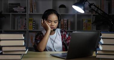Mujer cansada en auriculares y gafas aprendiendo con un portátil por la noche