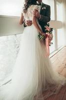 bride and groom with a wedding bouquet standing by the big window photo