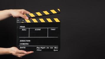 Hand is holding yellow and black clapperboard on black background. photo