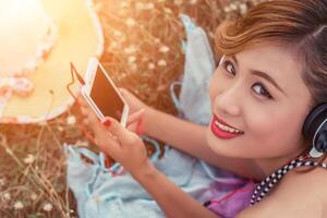 Sexy woman laying listening music from smartphone in the flower field. photo