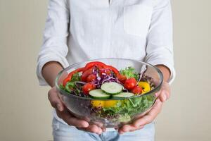 manos de mujer hermosa sosteniendo gran tazón de ensalada de verduras frescas. foto