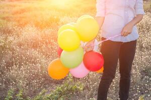 Manos de mujer hipster sosteniendo globos multicolores en los prados foto