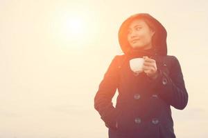 young woman wearing black coat holding a cup of coffee in the morning photo
