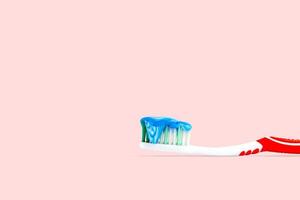 Blue and white toothpaste on a toothbrush on pink color background. photo