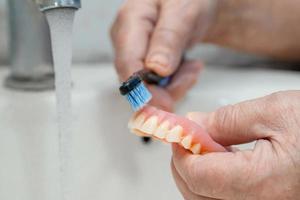 Paciente mujer mayor asiática usa cepillo de dientes para limpiar la dentadura parcial