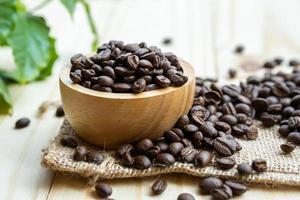 medio de grano de café tostado en un tazón de madera con hojas frescas por la mañana.