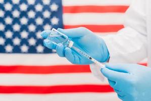 médico sosteniendo la botella de la vacuna y la jeringa con el fondo de la bandera de Estados Unidos. foto