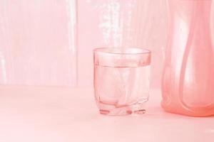 glass of water and plastic container on pink photo