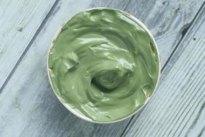 green clay mask in container on wooden background photo