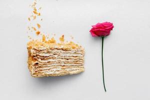 Piece of creamy cake with a rose on a white background. Top view photo