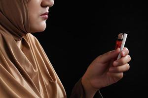 Cerrar joven mujer musulmana sosteniendo un cigarrillo sobre fondo negro foto