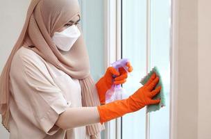 Mujer musulmana limpieza de vidrio de la puerta con tela y spray de alcohol
