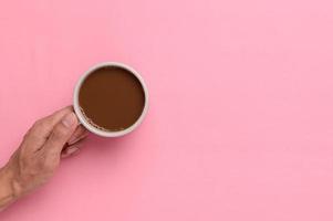 Hand holding a coffee mug on a pink background photo