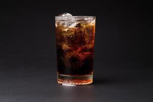 Cola en vaso con cubitos de hielo transparente aislado sobre fondo negro foto