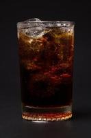 Cola en vaso con cubitos de hielo transparente aislado sobre fondo negro foto